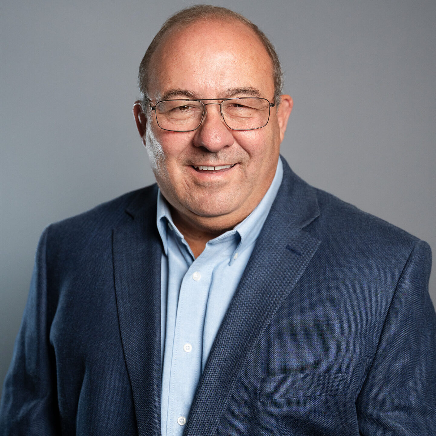 67f03f133cd33_About LPC_Meet The Team_Rodger Chase A man in a suit and glasses is smiling.