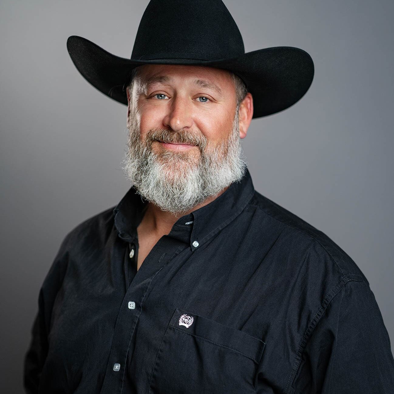 Chirs Hoff Man with a gray beard wearing a black cowboy hat and black button-up shirt, posing against a plain gray background.