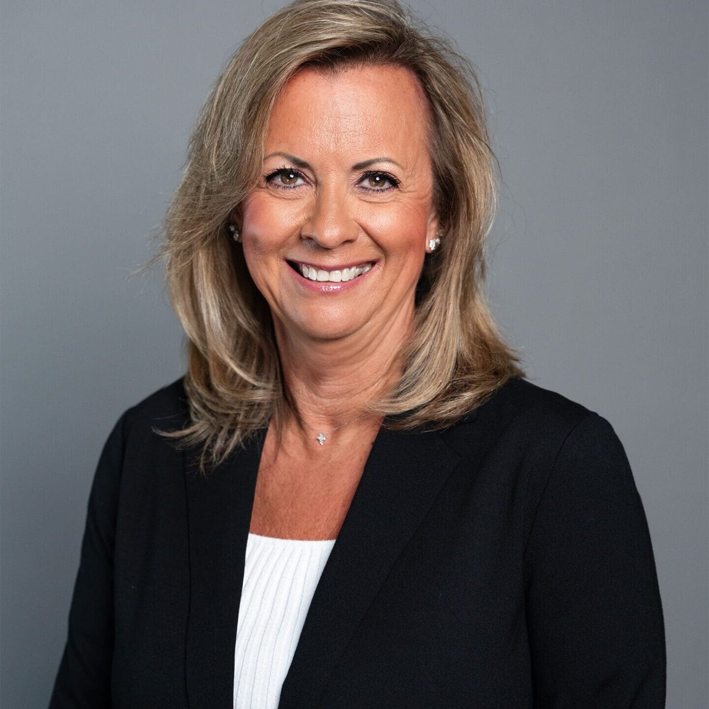 Diane Walters A woman with shoulder-length blonde hair wearing a black blazer over a white top, smiling in front of a plain gray background.